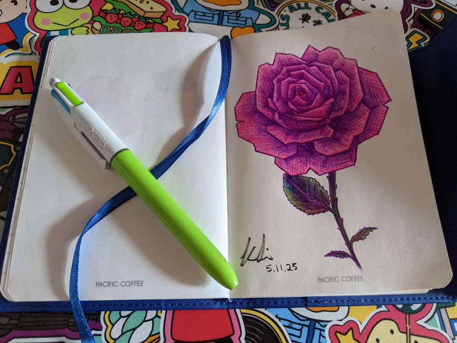 Purple rose drawing in an open sketchbook beside a pen